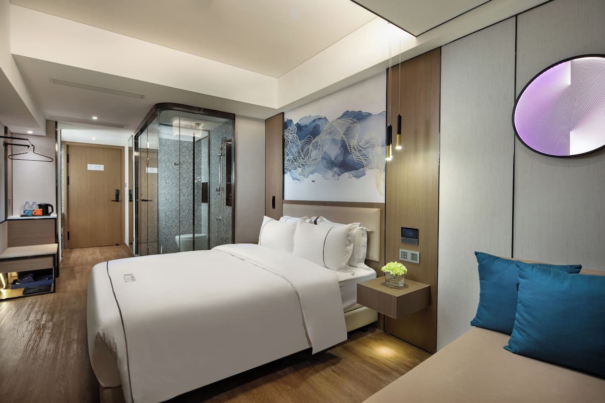 Une chambre d’hôtel moderne dotée d’un grand lit, de tables de chevet, d’un espace douche et d’une œuvre d’art accrochée au mur.