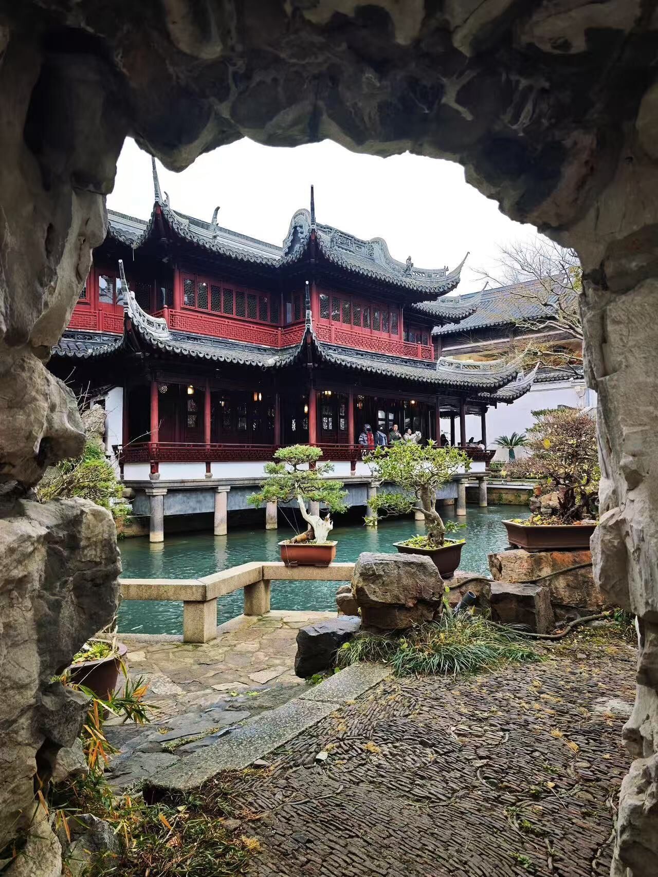 A traditional Chinese courtyard with a multi-tiered pavilion, stone lanterns, and bonsai trees.