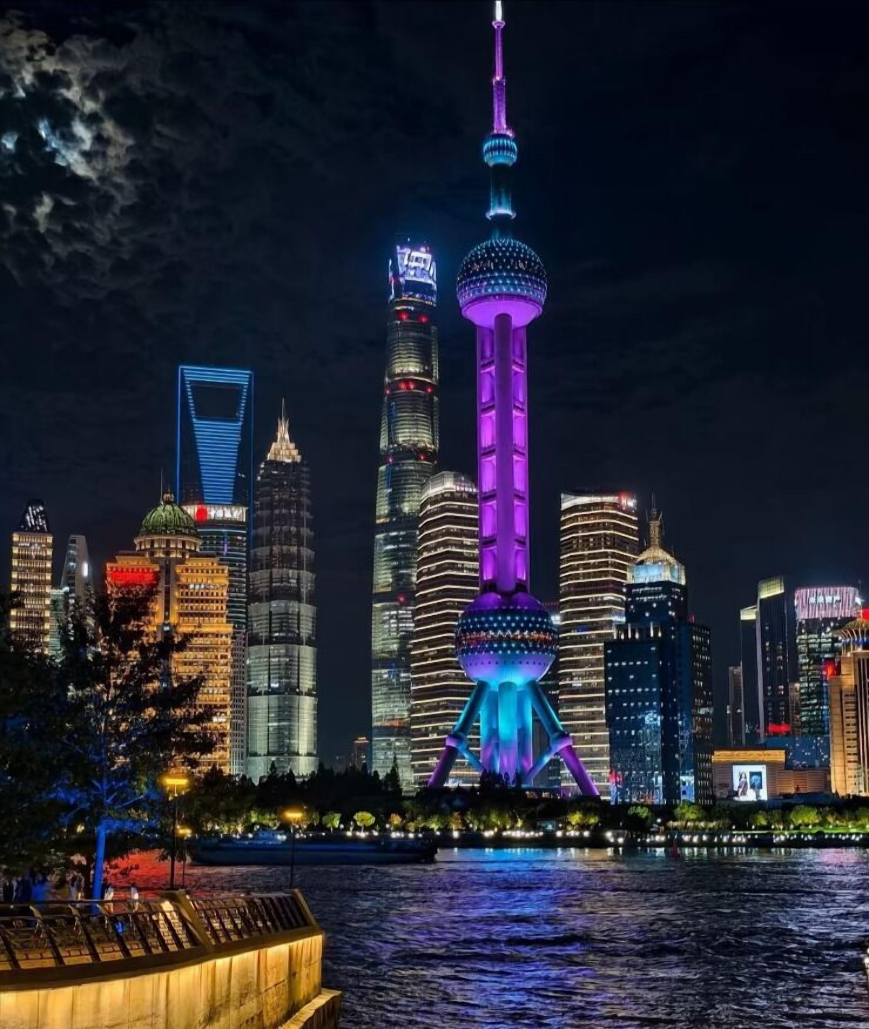 Un paisaje urbano nocturno con rascacielos iluminados y una torre destacada con una plataforma de observación esférica.