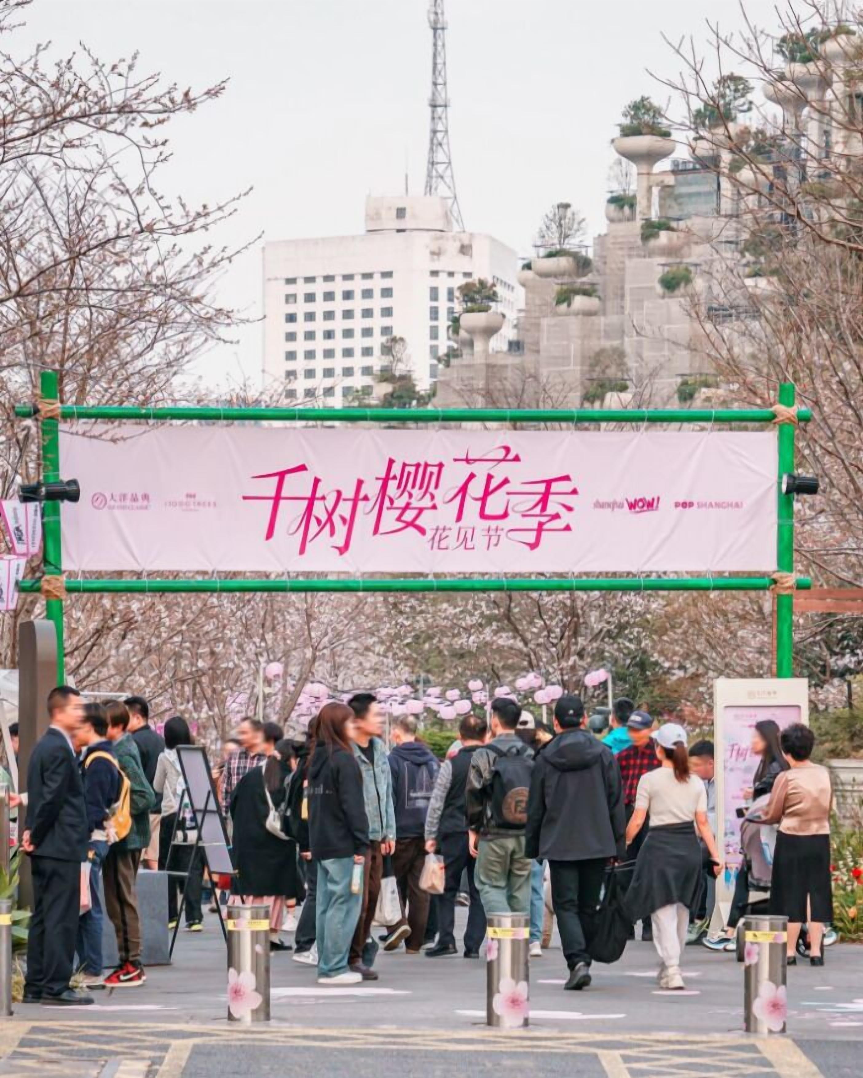 A crowd of people at an outdoor event with a banner displaying text in a foreign language.