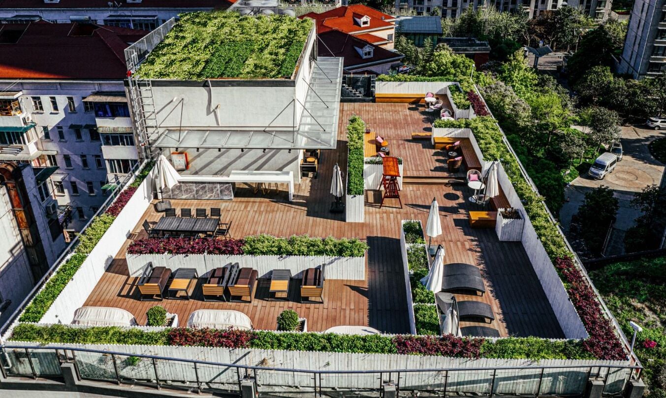 Vista aérea de um terraço com várias áreas de estar, um deck de madeira e vegetação ao redor.