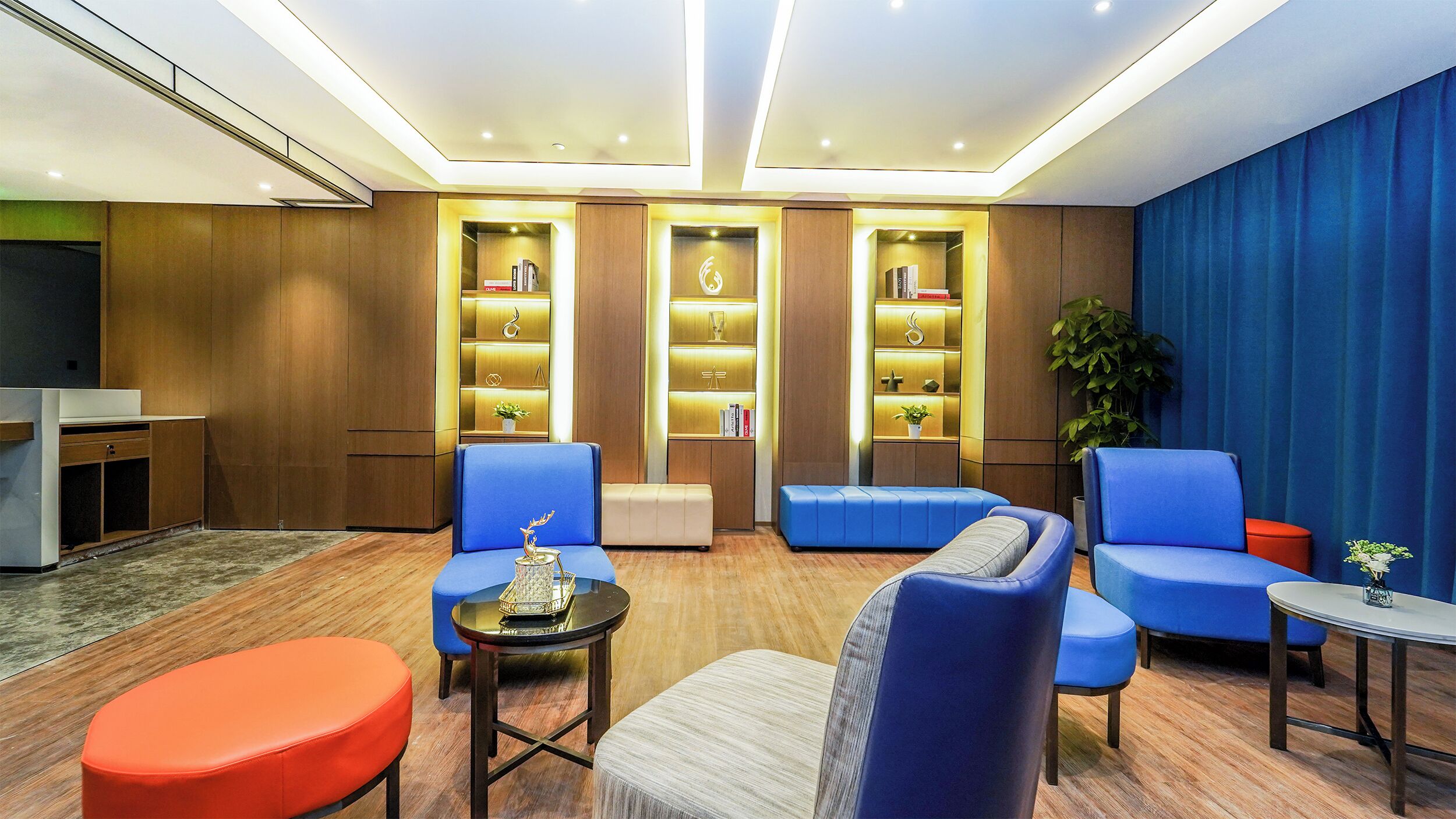 A modern living room with blue and orange seating, a small table, and a bookshelf with decorative items.