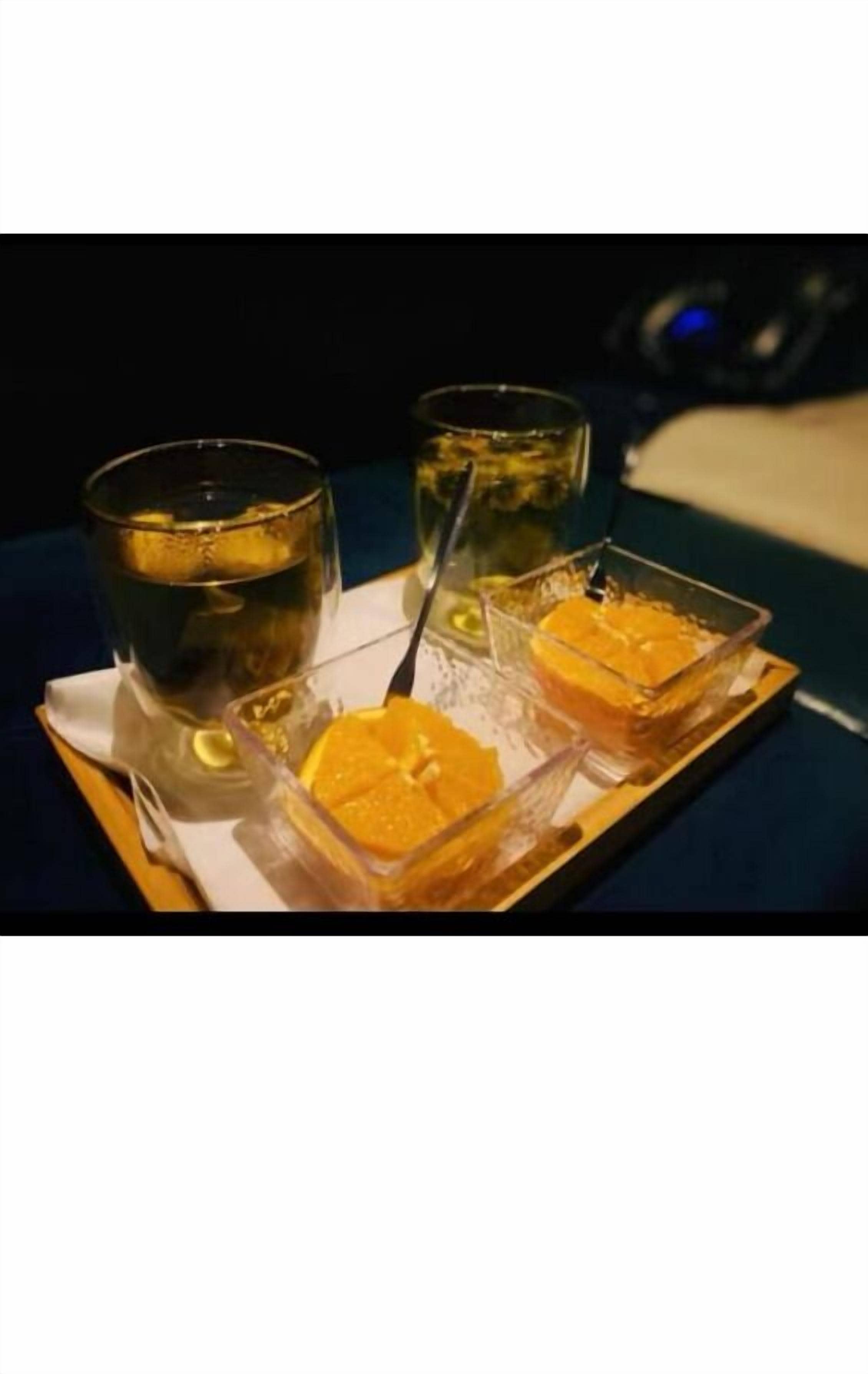 A tray with two glasses of a clear liquid and two small containers of a yellow substance, possibly food, on a dark tablecloth.