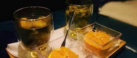 A tray with two glasses of a clear liquid and two small containers of a yellow substance, possibly food, on a dark tablecloth.