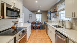 Una cocina moderna con armarios blancos, electrodomésticos de acero inoxidable y un comedor con mesa y sillas.