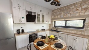 Cozinha moderna com armários brancos, parede de destaque em pedra, mesa de jantar com pratos pretos e janela com vista.