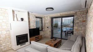 Uma sala de estar moderna com parede de pedra, televisão de tela plana, mesa de centro de madeira e sofá cinza.