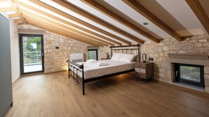 Quarto com parede de pedra, uma cama, mesa de cabeceira, janela e lareira.