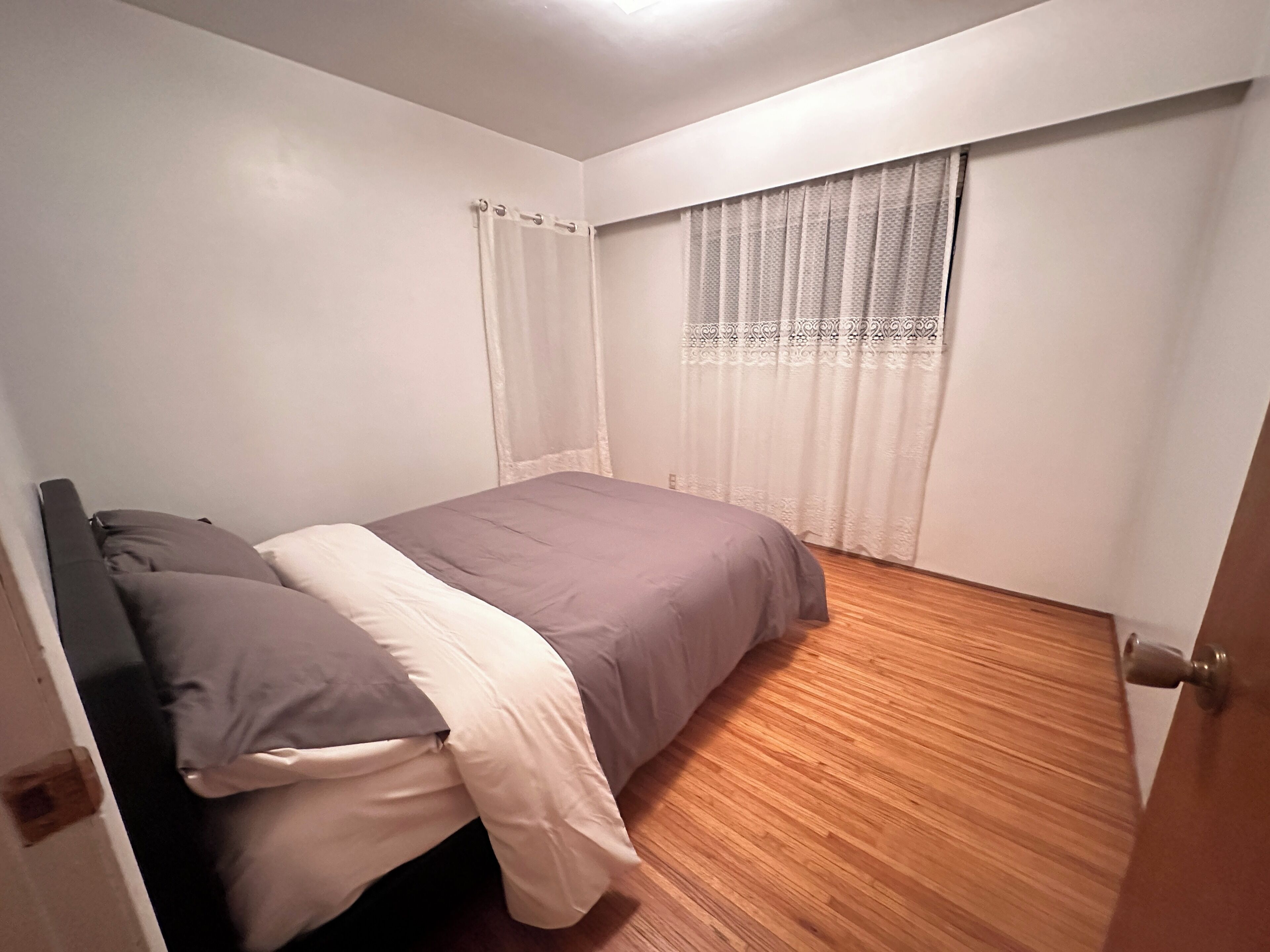 Une chambre à coucher avec un lit, une fenêtre ornée d’un rideau à motifs et un plancher en bois.
