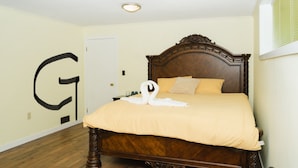 A bedroom with a wooden bed, a swan-shaped towel, and a large letter 'G' on the wall. - Spacious 8-bedroom house in gorgeous Richmond with AC (Richmond)