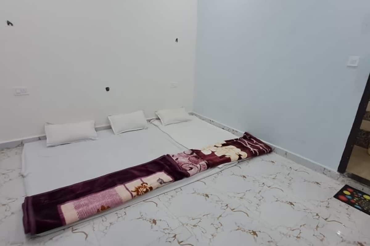 Una habitación pequeña y limpia con una cama individual, un tapete estampado y un baño visible a través de una puerta de cristal.