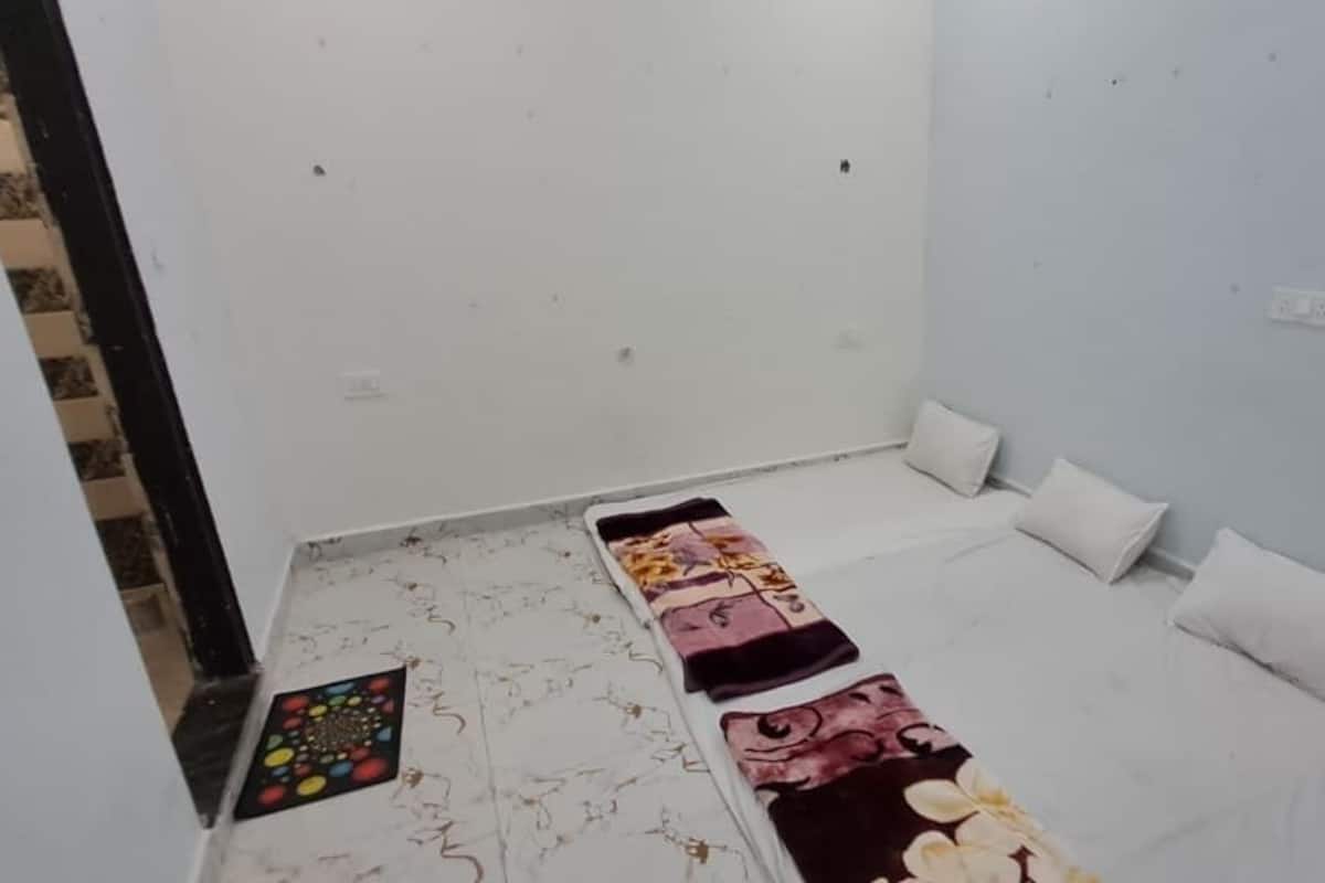 Una habitación pequeña y con pocos muebles, con una cama, almohadas, una manta y un felpudo en el suelo.