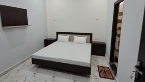 Ein Schlafzimmer mit einem Bett, einem Nachttisch, einem an der Wand montierten Fernseher und einer Badezimmertür.