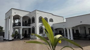 A large white building with multiple arches and balconies, surrounded by a courtyard with a tiled floor. - Miky Hillside Lodge (Sunyani)