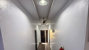 A narrow, well-lit hallway with a ceiling fan, a fire extinguisher, and a door at the end. - Miky Hillside Lodge (Sunyani)