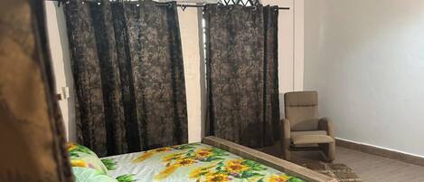 A bedroom with a bed, a chair, and a window with curtains.
