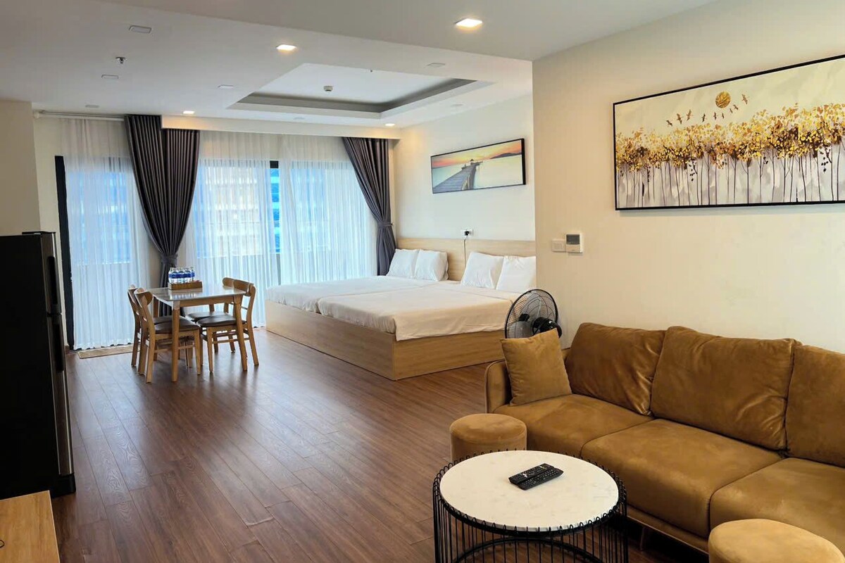 A hotel room with a bed, a sofa, a dining table with chairs, a TV, and a painting on the wall.