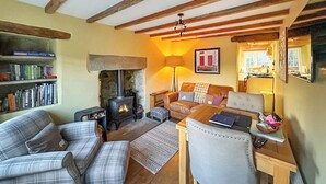 Una sala acogedora con chimenea, un sofá, una butaca, un escritorio y una estantería.
