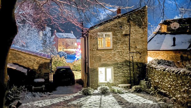 Un edificio de piedra con el suelo cubierto de nieve, un coche aparcado delante y una ventana visible.