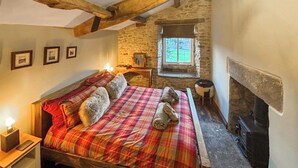 Un dormitorio acogedor con una cama de madera, una pared de piedra, un ventanal pequeño y una chimenea.