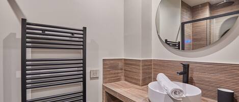 A modern bathroom with a towel rack, a sink with a round mirror, and a wooden textured wall.