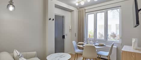 A modern living room with a sofa, dining table, chairs, and a small kitchen area.