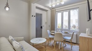 Ένα μοντέρνο σαλόνι με έναν καναπέ, ένα τραπέζι φαγητού, καρέκλες και μια μικρή κουζίνα με ένα καλοριφέρ.