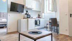 Et kompakt køkken med fjernsyn, mikrobølgeovn og kaffemaskine. Et spisebord med fjernbetjening ses i forgrunden.