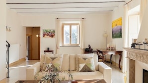 Uma sala de estar com sofá, mesa de centro com um vaso e objetos decorativos, lareira e um espaço de jantar com mesa e cadeiras.