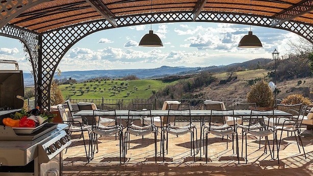 Um pátio externo com churrasqueira, cadeiras e vista para uma paisagem montanhosa.