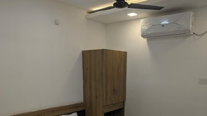 Een slaapkamer met een bed, een houten garderobe, een plafondventilator en een airconditioning.