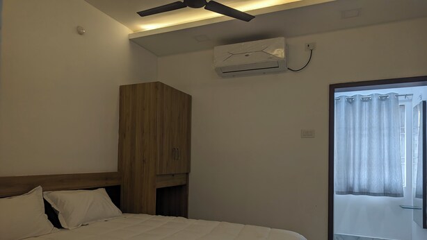 Een slaapkamer met een bed, een houten garderobe, een plafondventilator, een airconditioning en uitzicht naar buiten door een glazen deur.