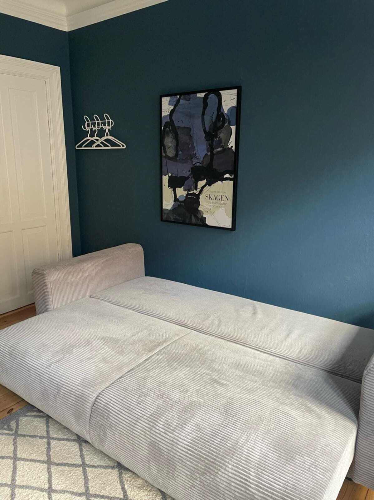 Una habitación con un sofá gris, una pared de acento azul y un cuadro abstracto enmarcado.