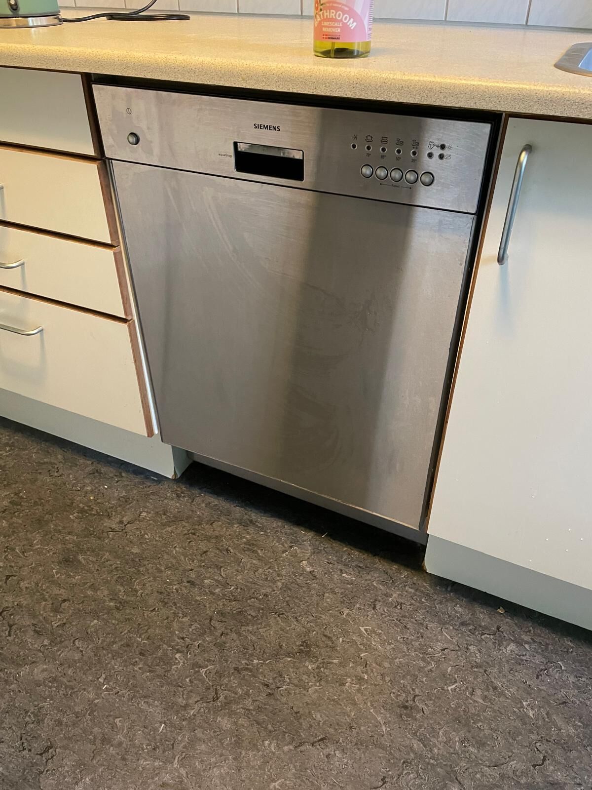 Un lavavajillas Siemens de acero inoxidable en una cocina con armarios blancos y encimera de granito.