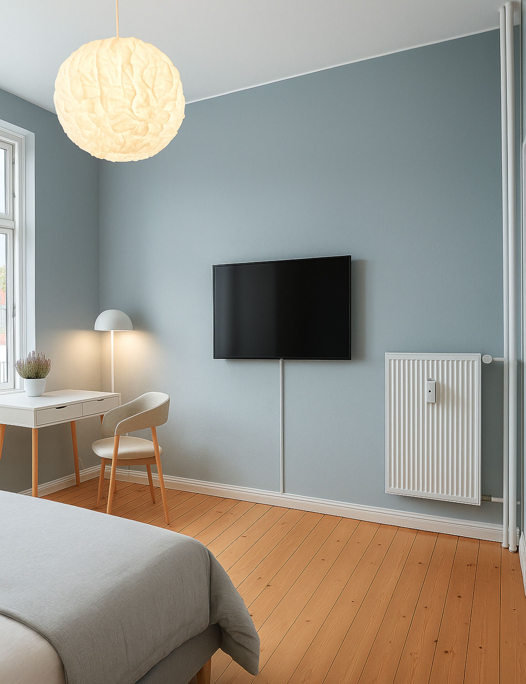 A modern bedroom with a bed, a desk, a chair, a television, and a radiator.