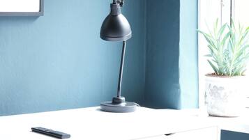 A desk with a lamp, a potted plant, and a framed picture on the wall.