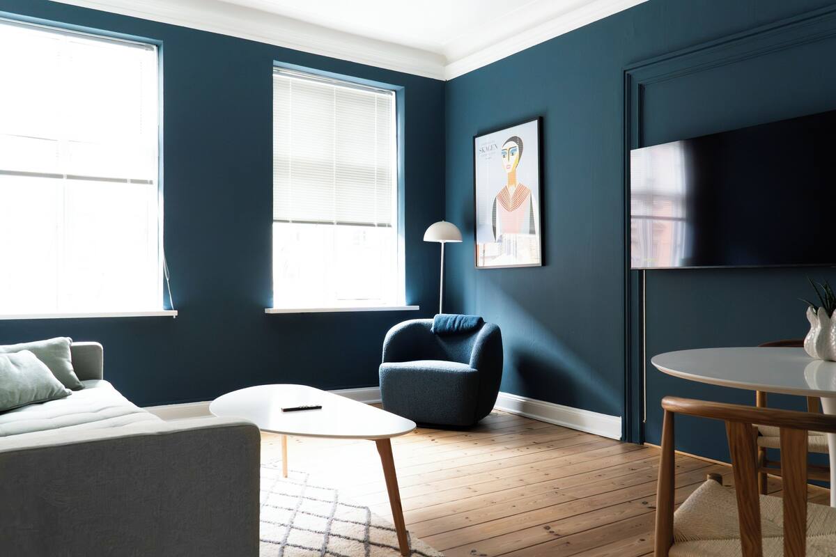 A modern living room with a sofa, armchair, round table, and a flat-screen TV.