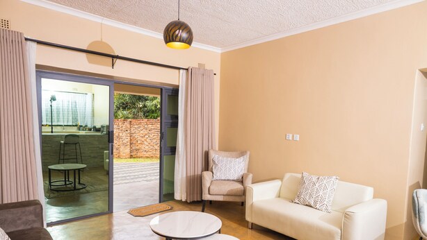 A modern living room with a sofa, armchair, and coffee table. There is a sliding glass door leading to an outdoor area. - Pabvute 8859 Apartments (Victoria Falls)