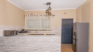 A kitchen with a marble countertop, a built-in microwave, a coffee maker, and a refrigerator. - Pabvute 8859 Apartments (Victoria Falls)