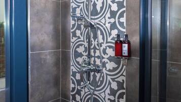 Um chuveiro com parede de azulejos estampados, porta de vidro e duas embalagens de shampoo.