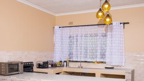 A compact kitchen with a central island, a microwave, a toaster, and a hanging light fixture. - Pabvute 8859 Apartments (Victoria Falls)