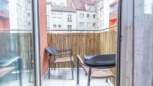 En balkong med utsikt över byggnader, ett bambustaket och två stolar samt ett bord.