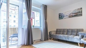 Ett modernt vardagsrum med en grå soffa, ett litet runt bord och ett stort fönster med gardiner.