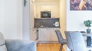 Ett kompakt kök med moderna vitvaror, en matplats med bord och stolar samt en stor växt på väggen.