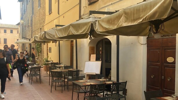 An outdoor café with tables and chairs, a whiteboard, and a door with a sign. - Locanda Il Pino (San Gimignano)