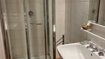 A modern bathroom with a glass-enclosed shower, a white sink with two faucets, and a mirror above the sink.