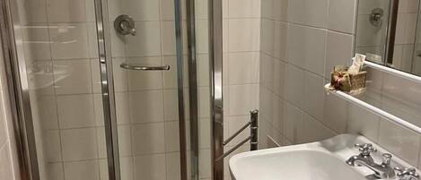 Un baño moderno con ducha envuelta en vidrio, un lavamanos blanco con dos grifos y un espejo sobre el lavamanos.
