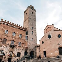 Un edificio storico con un'alta torre e un corpo più basso caratterizzato da finestre ad arco e una scala che conduce all'ingresso.