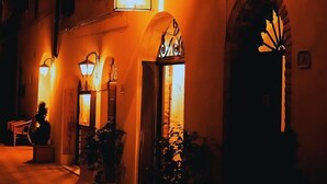 A warmly lit street with a building featuring arched doorways and a sign above the entrance. - Locanda Il Pino (San Gimignano)