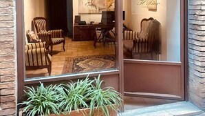 A modern interior with a large glass door, a seating area with striped chairs, a desk, and a decorative wall with a logo. - Locanda Il Pino (San Gimignano)